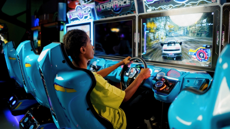 A vibrant arcade at Epic Waters Waterpark, filled with colorful flashing lights and a variety of games, including claw machines, racing simulators, and basketball hoops. Guests of all ages enjoy the energetic atmosphere as they play and collect tickets for prizes.