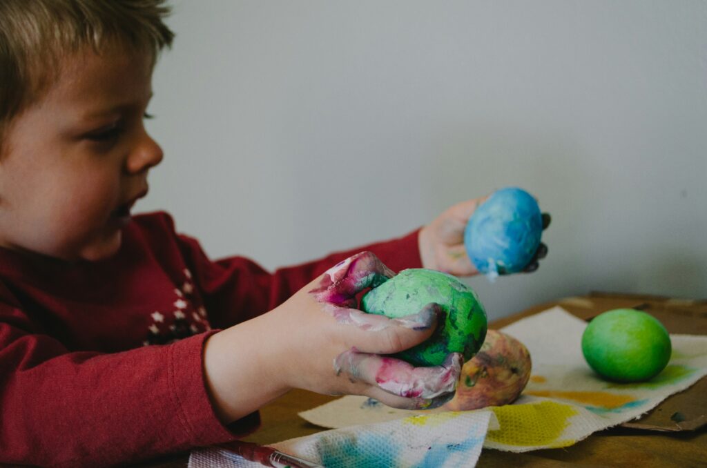 A little boy in a red shirt demonstrates one of the benefits of art for kids: discovery through play!