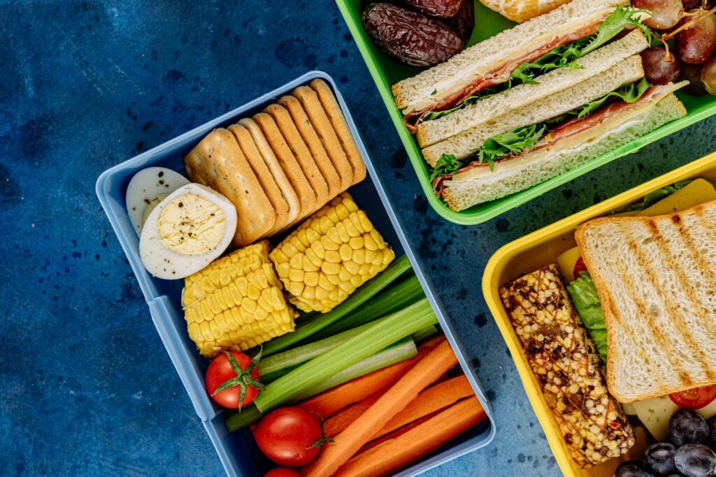 A colorful lunch box filled with sandwiches, fresh vegetables, and fruit, perfect for summer camp meals.