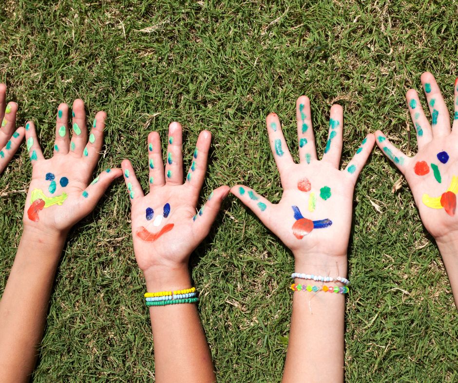 Colorfully painted hands placed on lush grass, representing artistic expression at a summer camp in Dallas.