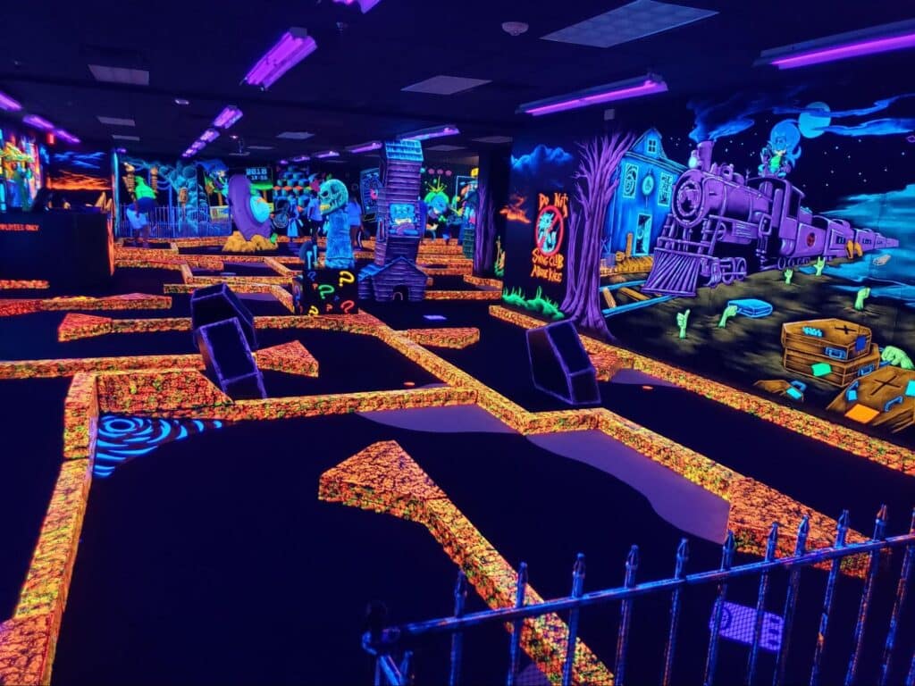 A colorful mini golf course featuring Halloween decorations and neon lights, ideal for kids' nighttime activities in Dallas.