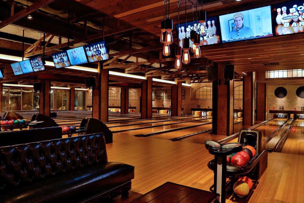 A lively bowling alley showcasing a large screen and a black couch, ideal for kid-friendly nighttime activities in Dallas.