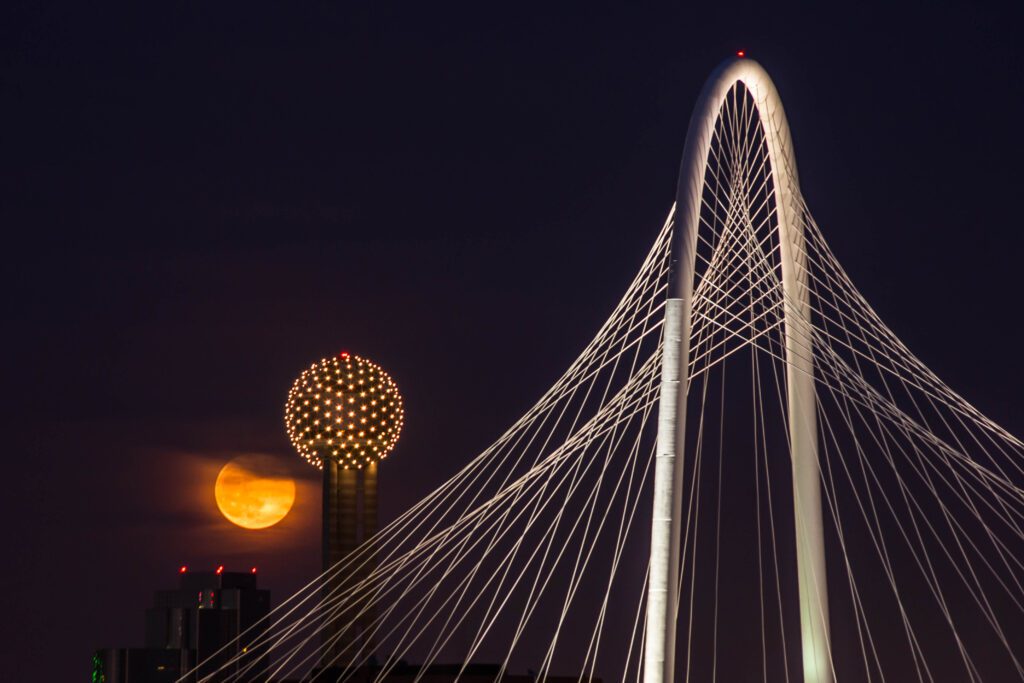 The moon gracefully descends behind a bridge, highlighting kid-friendly nighttime adventures in Dallas.