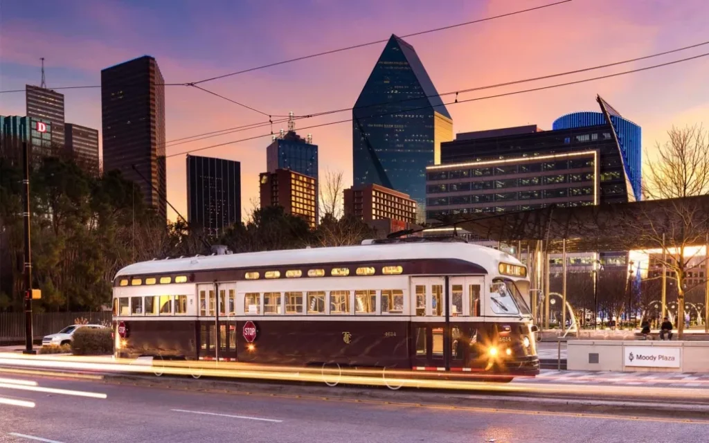 A trolley car moves along a city street, showcasing the vibrant nightlife of Dallas near McKinney Avenue.