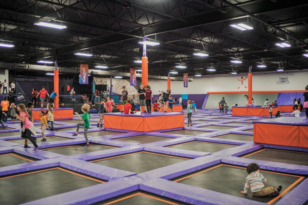 Families and children jump joyfully in a vibrant indoor trampoline park, a popular evening destination in Dallas.