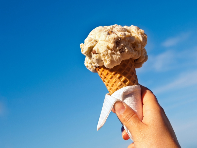  hand holds an ice cream cone, set against a vibrant blue sky