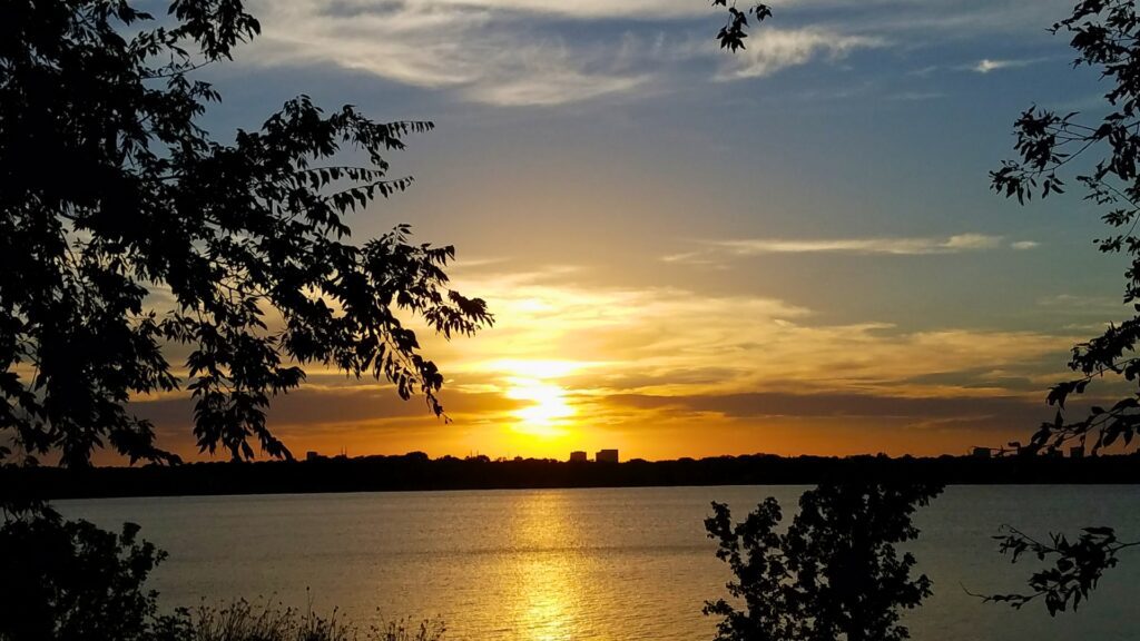 The sun sets over White Rock Lake, illuminating the sky with warm hues, perfect for a tranquil evening.