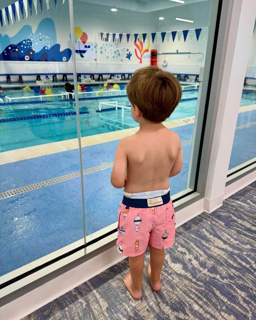 Little boy watches swim lessons through glass viewing area at Big Blue Swim School in Allen, Texas.